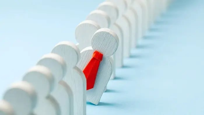 Wooden blocks shaped like people lined up with one leaning out wearing a red tie